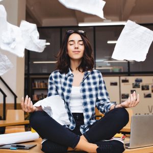 young pretty joyful brunette woman meditating on table surround work stuff and flying papers cheerful mood taking break working studying relaxation true emotions